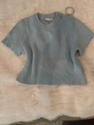 Ljusblå stickad topp från Zara - Supersöt ljusblå stickad topp från Zara med korta ärmar och rund hals. Toppen har ribbade detaljer vid ärmslut och nederkant, vilket ger en snygg och modern look. Perfekt att styla med jeans eller kjol för en fräsch outfit!! 🫰🏻✨(kan pruta ner priset)