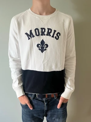 Vit och blå sweatshirt från Morris - Snygg sweatshirt från Morris i vitt och svart med broderad logga och text på bröstet. Tröjan har rund halsringning, långa ärmar och ribbade muddar. Perfekt för en avslappnad och trendig stil.