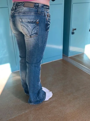 Blå bootcut jeans med detaljer - Säljer ett par blå bootcut jeans med slitningar och snygga sömmar på bakfickorna. Jeansen har låg midja.