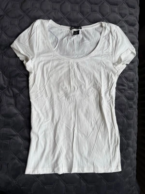 Vit basic t-shirt från H&M - En klassisk vit t-shirt från H&M Basic med rund halsringning och korta ärmar. T-shirten är i mjuk bomull och har en slim passform som sitter snyggt på kroppen. Perfekt att matcha med jeans eller kjol. Storlek xs