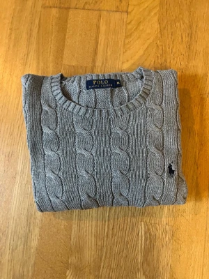 Polo Ralph Lauren Cable Knit – Grå | Strl M - Säljer en klassisk grå Polo Ralph Lauren Cable Knit med mörk logga. Stilren, lättmatchad och en garderobsklassiker. ✔️ Mycket fint skick ✔️ Storlek M ✔️ Mjuk och skön kvalitet ✔️ Tidlös design Finns även i marinblå – se gärna mina andra annonser. Paketpris vid köp av båda. Säljer då den är lite för bred för mig!