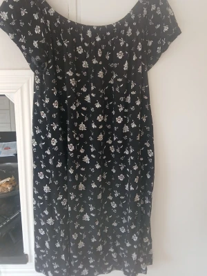 Svart blommig klänning med kort ärm - Söt svart klänning med vitt blommönster och korta ärmar. Klänningen har en avslappnad passform och rund halsringning. Perfekt för dig som gillar en enkel men stilren look.