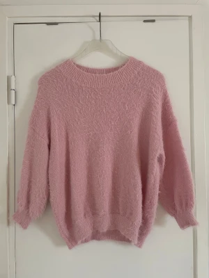 Ljusrosa stickad tröja - Supermjuk och fluffig stickad tröja i ljusrosa färg. Tröjan har rund halsringning, trekvartsärmar och ribbade muddar vid ärmslut och nederkant. 