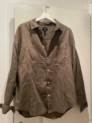 Grönbrun skjorta från H&M - Säljer en brun skjorta från H&M i avslappnad passform. Skjortan har långa ärmar, klassisk krage och knappar framtill. Tillverkad i ett mjukt bomullsmaterial som känns skönt mot huden. Den är helt oanvänd då den va för stor för mig