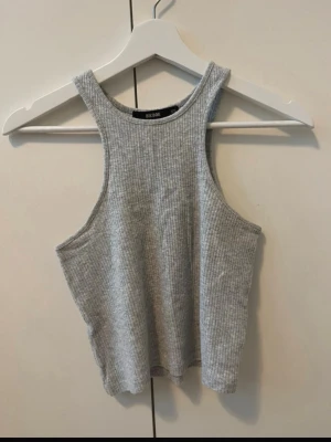 Grå ribbad linnetopp - Säljer en grå ribbad linnetopp med hög hals och ärmlös design. Toppen har en croppad passform och är tillverkad i ett mjukt, stretchigt material som passar perfekt till sommaren. Enkel och stilren, lätt att matcha med olika outfits.