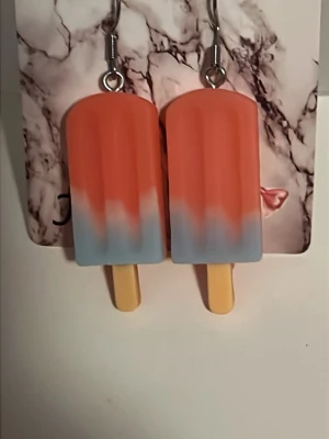 Örhängen i form av glasspinnar - Säljer ett par unika örhängen som ser ut som glasspinnar i rött, blått och vitt. De har en cool retrovibe och är tillverkade i plast med metallkrokar. Perfekta för dig som vill sticka ut och addera lite färg till din stil. Örhängens krokarna är i rostfritt stål.