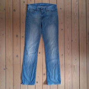Levi's Slight Curve Straight Jeans - Par ljusblåa jeans med rak passform och normal midja. Storlek W26 L32. Jeansen har ett väldigt litet blå märke på vänstra byxbenet (se bild 5 . Fållarna på byxbenen har slitagemärken (se bild 7). Midja ca 72 cm. Benlängd ca 73,5 cm.