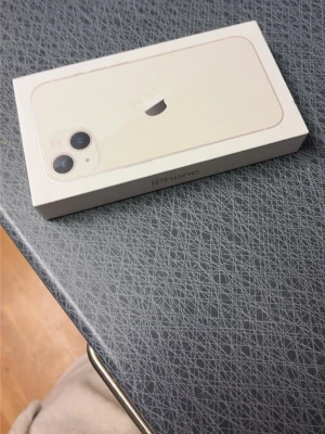 Vit iPhone 13 - Säljer en vit iPhone med stilren design och två kameror på baksidan. Telefonen har en slimmad form och levereras i originalförpackning. Perfekt för dig som gillar snygg teknik och vill ha en modern smartphone i klassisk färg.