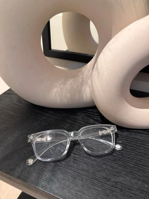 Transparenta chrome hearts glasögon med fyrkantig form - Säljer ett par stilrena chrome heart glasögon med transparent båge och fyrkantig form. Bågarna har coola detaljer vid gångjärnen och ger en modern vibe till din look. Perfekta för dig som vill ha något cleant och trendigt.
