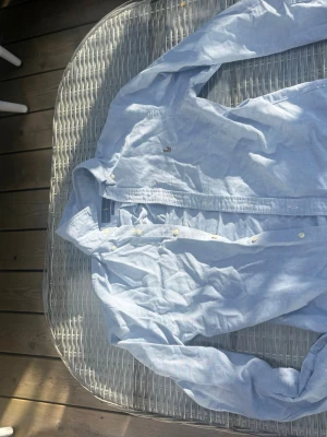 Ljusblå skjorta från Ralph Lauren - Säljer en ljusblå skjorta från Ralph Lauren i slim fit. Skjortan är tillverkad i bomull, har långa ärmar och klassisk krage. Detaljer som knappar framtill och den ikoniska broderade loggan på bröstet. Perfekt för en clean och stilren look.