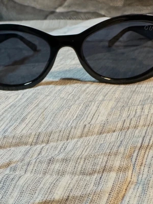 Svarta solglasögon från Gucci - Snygga svarta solglasögon från Gucci med ovala glas och breda skalmar. På sidorna finns den ikoniska dubbla G-loggan i silver. Glasögonen har en klassisk och trendig look som passar perfekt till sommaren.