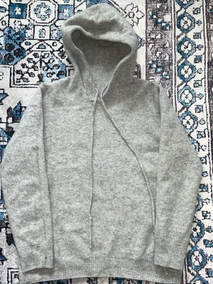 Ljusgrå hoodie med dragsko - Mysig ljusgrå hoodie i mjukt material med huva och långa ärmar. Klass modell med ribbade muddar och dragsko i halsen. Perfekt för chill dagar eller när du vill ha något enkelt och stilrent. Skön och stretchig 