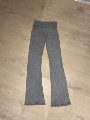 Grå ribbade mjukisbyxor Gina Tricot - Mysiga grå mjukisbyxor från Gina Tricot med bred ribbad midja och ut svängda ben. Tillverkade i mjukt stickat material som känns skönt mot huden. Perfekta för chill dagar hemma eller när du vill vara extra bekväm.