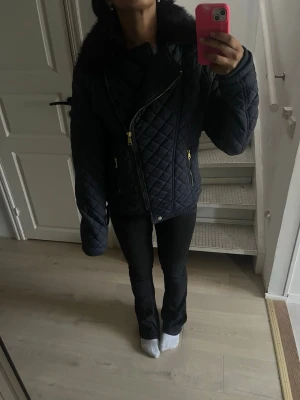 Marinblå jacka med svart pläs  - Säljer en svart quiltad jacka med sned dragkedja och stor krage i fuskpäls. Jackan har guldfärgade detaljer och en figurnära passform. Perfekt för dig som vill ha en snygg och trendig jacka till höst och vinter. Storlek Xxl men passar som M/S skulle jag säga själv har jag xs i kläder så den är verkligen inte Xxl🥰