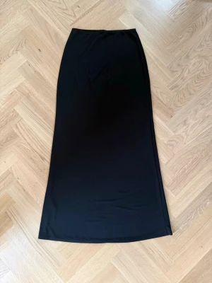 Svart långkjol från Gina Tricot - Säljer en svart långkjol från Gina Tricot. Kjolen har en enkel och stilren design med rak passform och är gjord i ett mjukt, stretchigt material som känns bekvämt mot huden. 