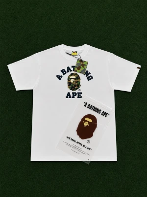 Vit BAPE t-shirt med camo-logga - Det här är en vit bape t-shirt med camo tryck på bröstet, bape är det tyngsta streetwear märket just nu så om du vill sticka ut i mängden är denhär perfekt för dig. Storlek M. 100% bomull så du har en skön och luftig t-shirt. Påse och tags följer med vid köp! 