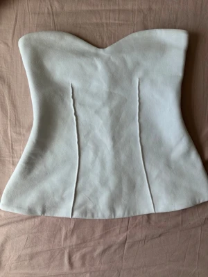 Vit axelbandslös topp - Snygg vit topp med hjärtformad urringning och figurnära passform. Axelbandslös design som ger en clean och stilren look. Materialet ser ut att vara mjukt och något stretchigt, perfekt för att styla med jeans eller kjol.