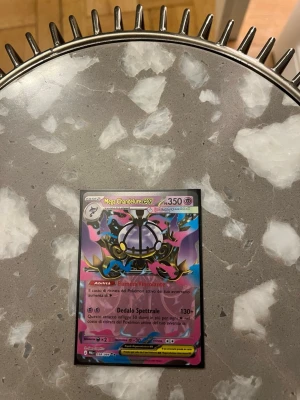 Pokémonkort Mega Chandelure EX - Säljer ett Pokémonkort med motivet Mega Chandelure EX. Kortet har färgstark design i lila, blått, svart och gult med holografiska detaljer. Texten på kortet är på italienska och det har 350 HP. Perfekt för samlare eller dig som vill utöka din Pokémonkort-lek. Den är i en plastfika så man får med plastfika 