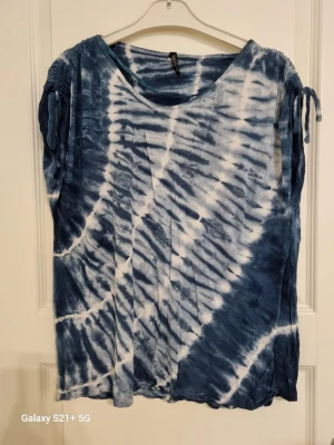 Blåvit batik topp med knytärmar - Säljer en loose fit topp i blått och vitt batikmönster. Toppen har rund halsringning och korta ärmar med snygga knyt-detaljer upptill. Perfekt för dig som gillar avslappnad och unik stil.
