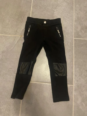Svarta leggings med skinndetaljer H&M - Snygga svarta leggings från H&M med coola skinndetaljer på knäna och dragkedjor vid fickorna. Stretchigt material som sitter skönt och ger en trendig look. Perfekta till en streetstyle-outfit eller när du vill ha något extra.