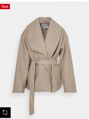 Beige kappa med skärp från ONLY - Stilren beige kappa från ONLY med bred sjalkrage och knytskärp i midjan. Köpt för 679 kr.Kappan har en avslappnad passform och är tillverkad i ett mjukt, ull-liknande material. Perfekt för lager på lager och ger en trendig look till alla outfits.