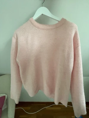 Ljusrosa stickad tröja - Mysig ljusrosa stickad tröja med rund halsringning och långa ärmar. Tröjan har en enkel, avslappnad passform och är tillverkad i ett mjukt material som känns skönt mot huden. Perfekt för kyliga dagar och enkel att matcha med olika outfits.