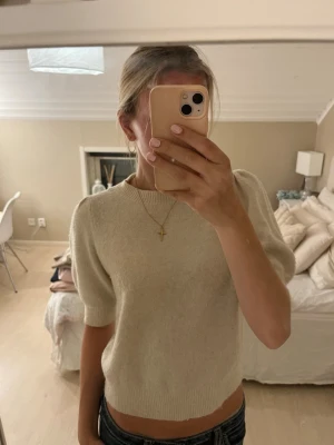 Stickad tröja med puffärm - Säljer en mjuk och stilren beige stickad tröja med puffärm och ribbade muddar. Tröjan har rund halsringning och kortare ärmar som ger en trendig look. Tröjan är nopprig men fortfarande snygg och bekväm💗