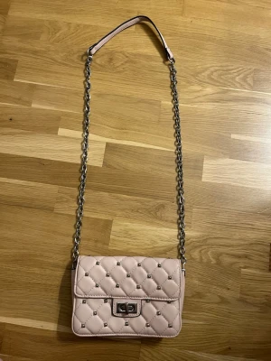 Rosa handväska - Ljusrosa handväska med metall pigg-detaljer, ett litet slitage på baksidan som syns på sista bilden💕 Spännet på framsidan har tappat lite färg men funkar att vrida som vanligt!!