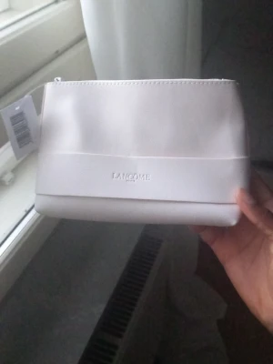 Lancôme necessär och ansiktskräm - Säljer en stilren, ljusrosa necessär från Lancôme i slätt material med mini hudvårdsprodukter. Perfekt för att organisera dina skönhetsprodukter och ta hand om huden.