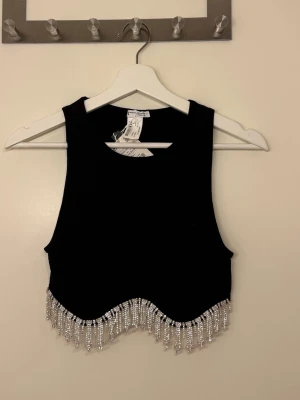 Svart topp med glitter detaljer - Svart topp med glitter detaljer från Zara i storlek XS-S. Endast testad med prislapp kvar. Dock är det en liten sten som ramlat av (se bild) men inte synligt från långt håll.