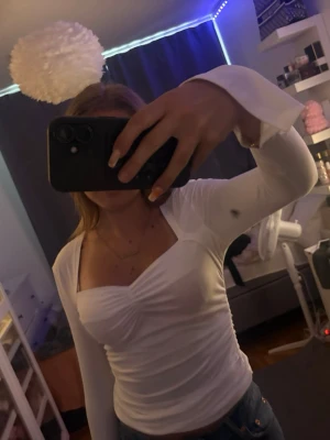 Vit långärmad topp med rynk - Säljer en vit långärmad topp med fyrkantig ringning och rynkdetalj framtill. Toppen är figurnära och har långa ärmar med lätt utsvängd kant. Perfekt att styla med jeans eller kjol för en trendig look. Aldrig använd!💞💞