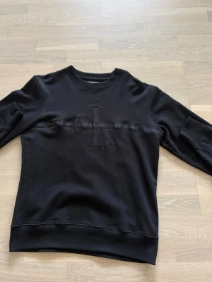 Svart sweatshirt från Calvin Klein - Säljer nu min snygga CK jeans tröja. Passar till allt och har en snygg logga som smälter in perfekt med den svarta tröjan! Den är i storlek S men passar perfekt på mig som använder M 
