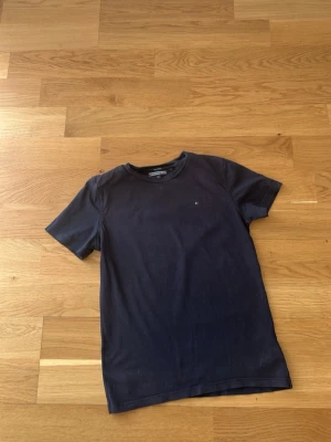 Mörkblå Tommy hilfiger  t-shirt  - En stilren mörkblå t-shirt med rund hals och korta ärmar. På bröstet finns en liten diskret logga i rött, vitt och blått. Perfekt för en enkel och clean look. Tillverkad i mjuk bomull som känns skön mot huden.