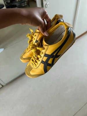 Gula Onitsuka Tiger Mexico 66 sneakers - Snygga gula Onitsuka Tiger Mexico 66 sneakers med svarta detaljer och klassiska stripes på sidorna. Skorna är i superbra skick! Nypris: 1800kr