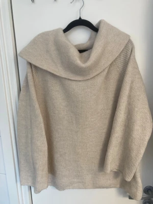 Beige stickad tröja strl L  - Mysig beige stickad tröja med bred, nedvikt krage och långa ärmar. Tröjan har en avslappnad passform och är ribbstickad i ett mjukt material, perfekt för kyliga dagar. Enkel och stilren design som passar till det mesta. Inga hål eller fläckar! 