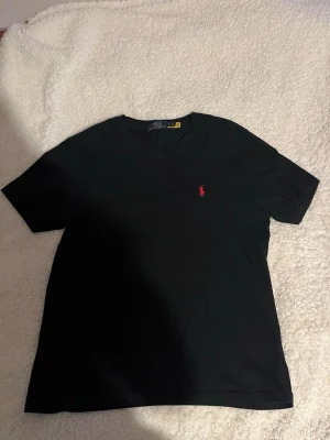 Polo Ralph Lauren T-shirt - Klassisk svart t-shirt från Polo Ralph Lauren med röd broderad logga på bröstet. T-shirten har rund halsringning och korta ärmar. Perfekt basplagg som funkar till allt och är tillverkad i mjuk bomull.