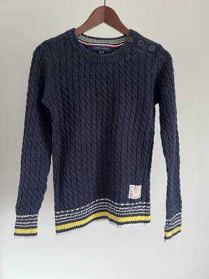 Tommy Hilfiger Kabelstickad tröja (Cable Knit Sweater) - Tommy Hilfiger Kabelstickad tröja (Cable Knit Sweater) Storlek: S Färg: Marinblå med vit-, grå- och gula ränder vid muddarna Passform: Regular fit Krage: Rund hals (Crew Neck) Material: Bomull & Nylon Skick: Denna tröjan är i ett väldigt fint skick utan defekter  Nypris cirka: 1 200 kr