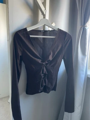 Brun topp - Trendig brun croppad topp med lång ärm. Toppen har v-ringning och öppna partier. Perfekt för dig som vill sticka ut och matcha med höga jeans eller kjol. 