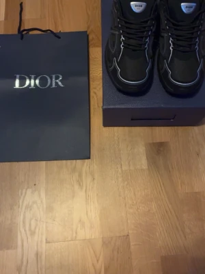 Svarta Dior B30  - Snygga svarta Dior sneakers med vita kontrastsömmar och logga på plösen. Skorna har  klassisk snörning. Materialet ser ut att vara en mix av textil och läder för en exklusiv känsla. Perfekta för dig som vill sticka ut med stil. Skorna har ALDRIG använts helt nya från boxen. Kom dm för mer bilder 