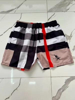 Rutig shorts med snörning - Snygga shorts med rutigt mönster i svart, vitt, beige och rött. De har elastisk midja med snörning och sidofickor. Perfekta för sommaren och ger en trendig look. lite kortare i längden passar någon runt 175cm.