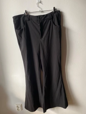 Svarta vida kostymbyxor - Snygga svarta kostymbyxor med vida ben och hög midja. Byxorna har bälteshällor, knapp och dragkedja framtill samt två fickor. Perfekta för en clean och stilren look.
