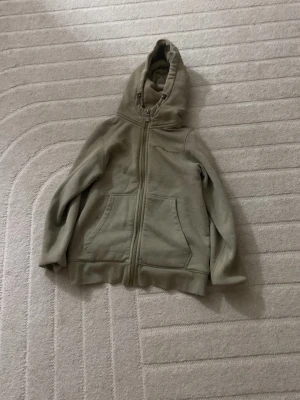 Beige hoodie från Sail Racing - Snygg beige hoodie från Sail Racing med dragkedja framtill och två stora fickor. Hoodien har broderad logga på bröstet och en klassisk huva. Tillverkad i mjukt material som känns skönt mot huden. Perfekt för en avslappnad stil.