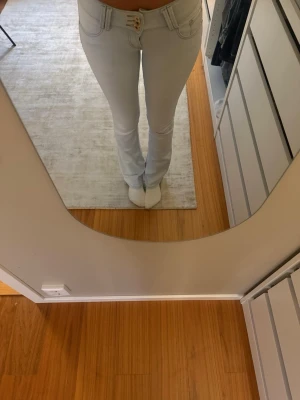 Ljusblå bootcut jeans med låg midja - Säljer ett par ljusblå jeans med hög midja och bootcut-modell. Jeansen har tre knappar framtill, klassiska fickor och är tillverkade i ett stretchigt denimtyg. Använda 1-3 gånger så i väldigt bra skick!