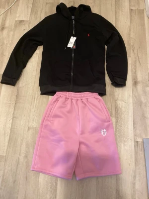  Polo Ralph Lauren Zip-up Hoodie +Rosa Sweatshorts  -  Polo Ralph Lauren Zip-Up Hoodie + Rosa Sweatshorts   Säljer en stilren Polo Ralph Lauren zip-up hoodie och ett par rosa premium sweatshorts. Plaggen säljs både separat och tillsammans.  Priser: • Hoodie: 600 kr • Shorts: 380 kr • Paketpris: 820 kr (du sparar 160 kr!)  Perfekt för dig som vill ha en snygg och bekväm outfit. Båda plaggen är i fint skick.  Skriv om du vill ha fler bilder eller har några frågor!