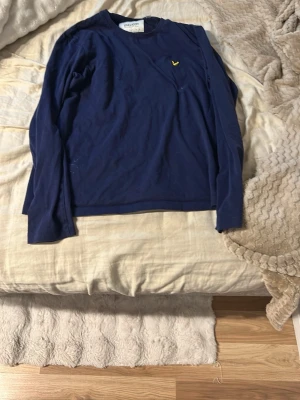 Mörkblå långärmad tröja Lyle & Scott - Mörkblå långärmad tröja från Lyle & Scott med rund halsringning och den klassiska gula logon broderad på bröstet. Tillverkad i mjukt bomullsmaterial som känns skönt mot huden. Perfekt till jeans eller chinos för en enkel och stilren look.