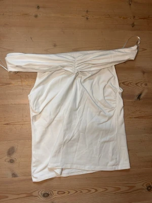Vit offshoulder topp med rynk - Trendig vit offshoulder topp med rynkdetalj framtill. Toppen är ärmlös och har en axelbandslös design som ger en snygg och modern look. Tillverkad i mjukt bomullsmaterial som känns bekvämt mot huden. Perfekt för dig som vill ha en stilren och enkel topp.