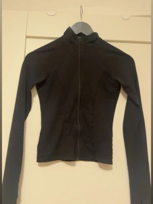 Svart ziptröja från Gina Tricot - Svart långärmad ziptröja från Gina Tricot i figurnära modell. Tröjan har hel dragkedja framtill och hög krage!