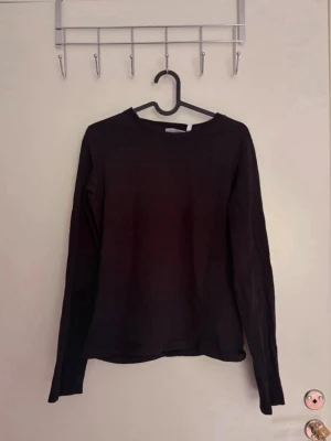 Svart långärmad topp - En enkel svart långärmad topp med rund halsringning. Perfekt basplagg som funkar till det mesta och är lätt att styla med olika outfits. Tillverkad i mjukt material för en bekväm känsla.