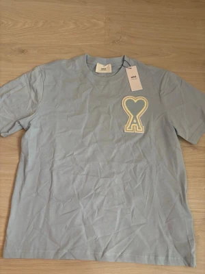 Ljusblå t-shirt från Ami Paris - Snygg ljusblå t-shirt från Ami Paris med ett stort broderat hjärta på bröstet. Klassisk passform och rund halsringning. Perfekt för dig som vill ha en enkel men ändå unik look.