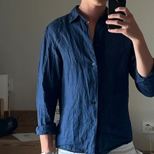 Blå linneskjorta från Uniqlo  - Snygg blå skjorta från Uniqlo i luftig linne, perfekt för dig som gillar en avslappnad men stilren look. Skjortan har klassisk krage, knäppning framtill och långa ärmar. Enkel att matcha med både jeans och shorts.